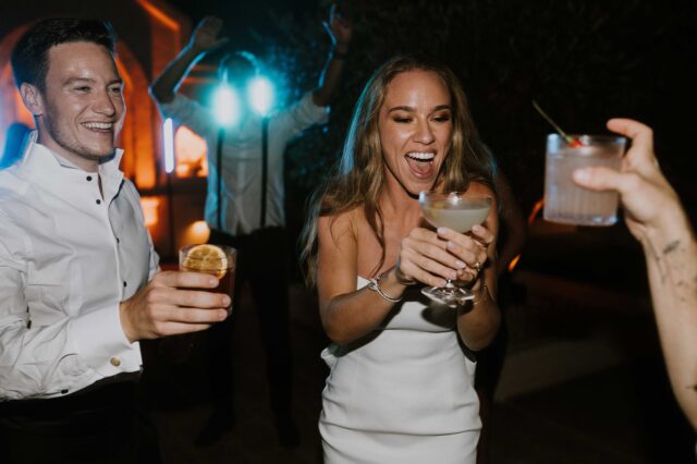 Persone che brindano e sorridono durante una festa, con drink in mano e un'atmosfera vivace